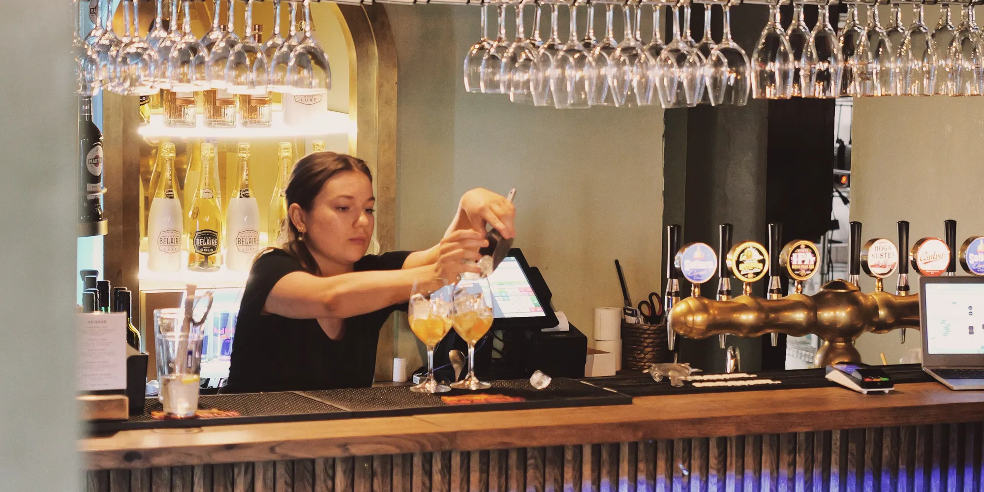 Bartendern häller upp en drink bakom baren under de hängande glasen