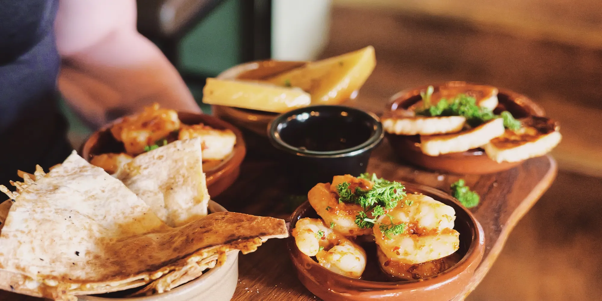 En servitör bär en träbricka med tapas i terrakottaskålar genom salen