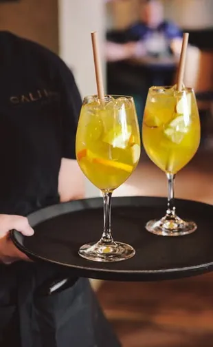 Två gula spritzdrinkar på en bricka som en servitör bär