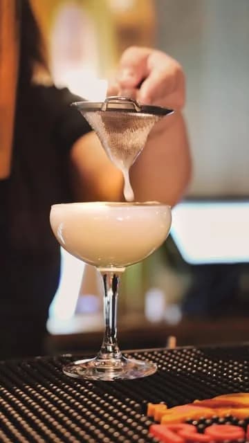 Bartender som silar en krämig sour i en coupeglas