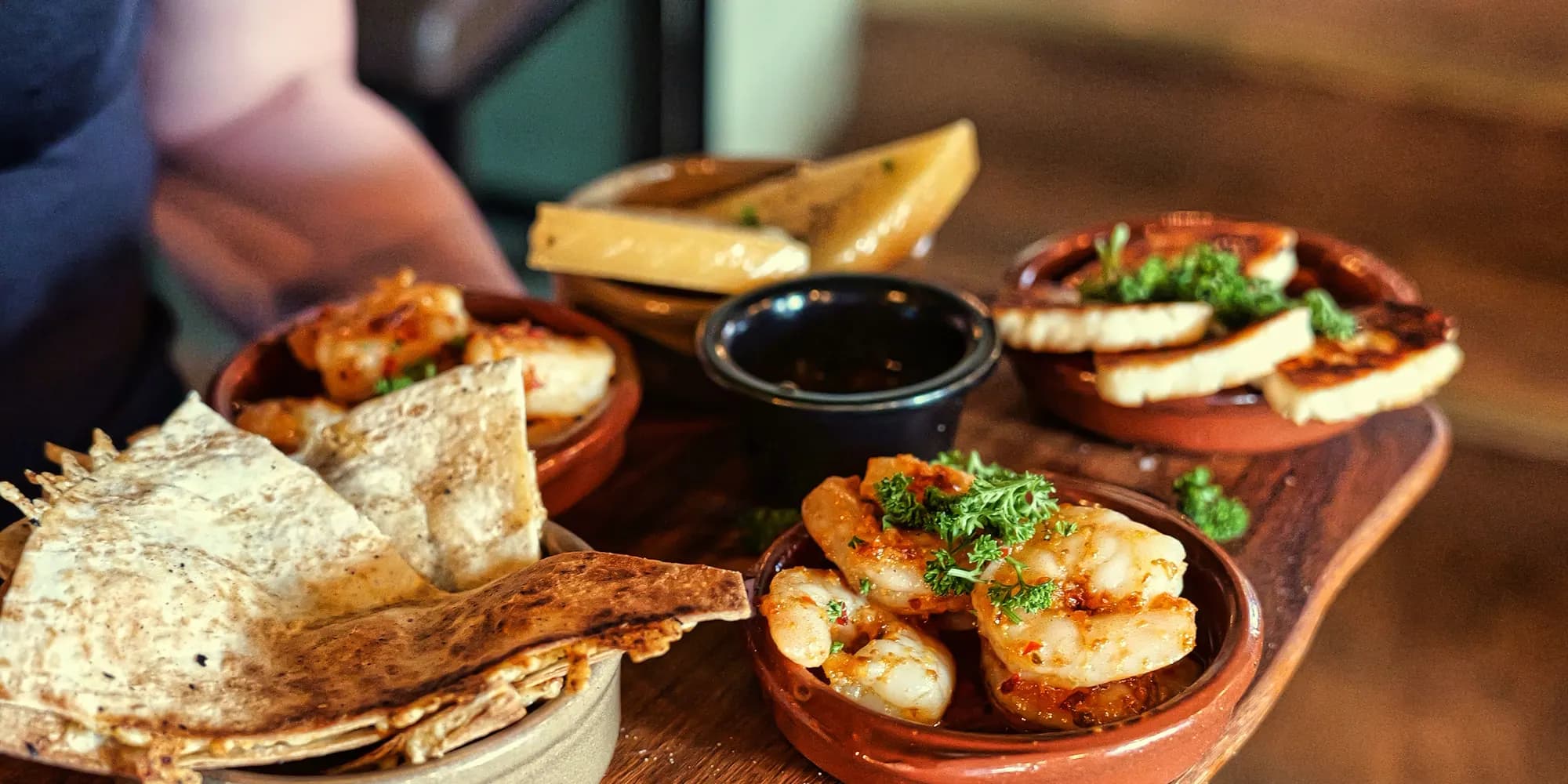 En träbricka med tapas: bröd, räkor, aioli och grillade grönsaker i terrakottaskålar