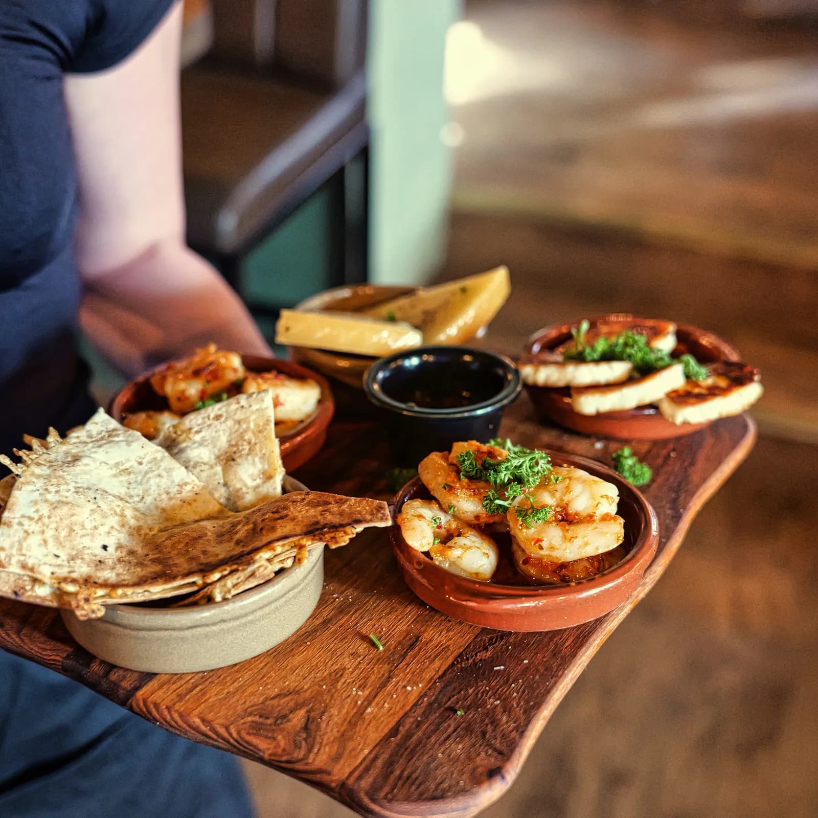 En servitör bär en träbricka med tapas i terrakottaskålar genom salen